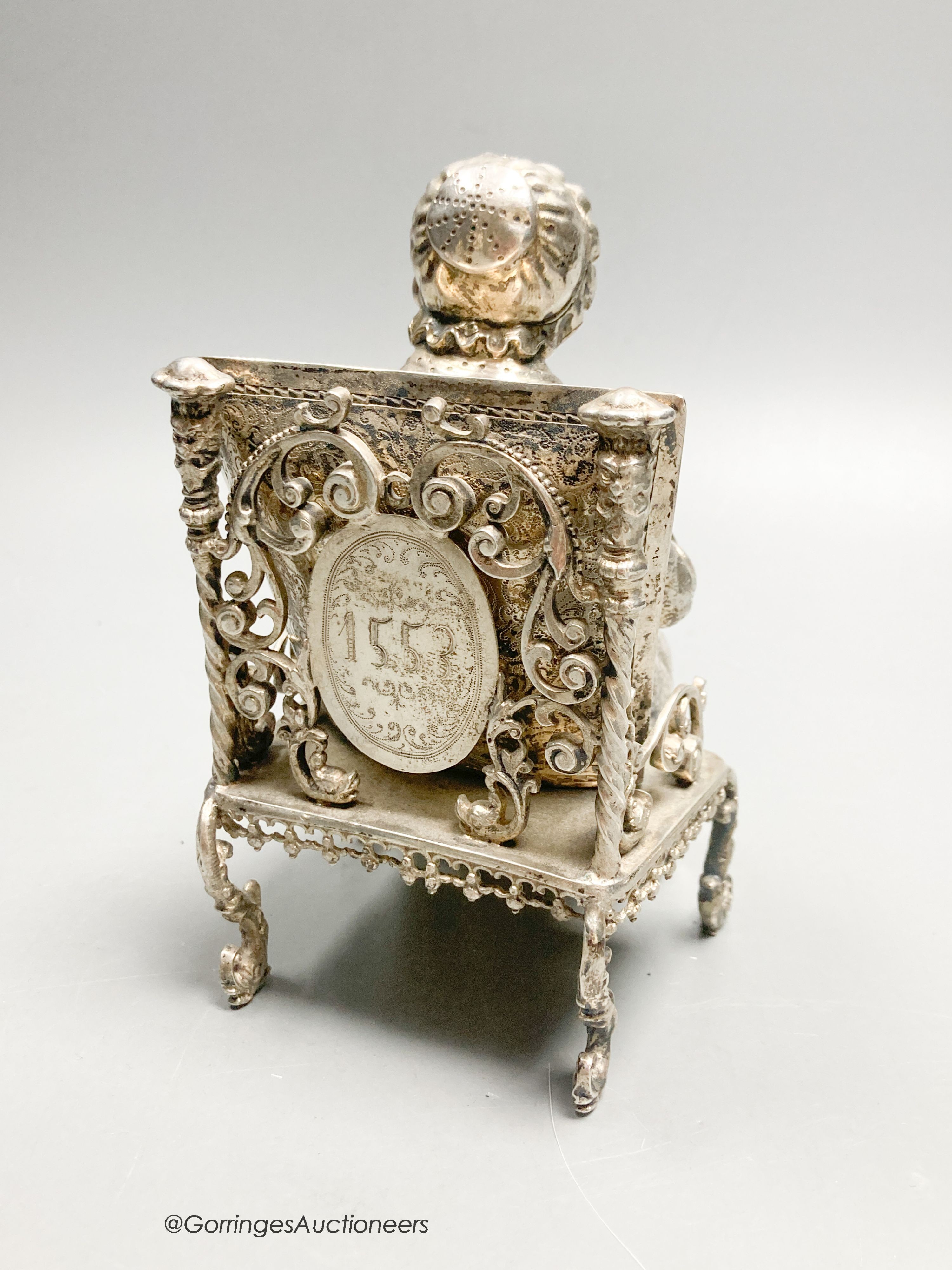 A late 19th century Hanau? white metal miniature model of an elderly lady seated in an armchair with cushion, engraved verso '1553, height 13.5cm